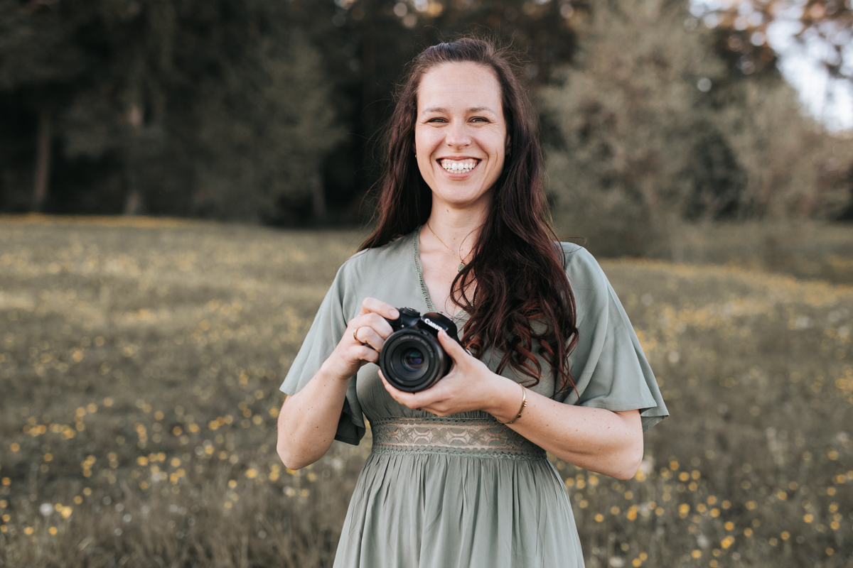 Eine junge Fotografin mit ihrer Kamera. Sie blickt durch den Sucher. Hinter ihr glitzert die goldene Sonne in den Blättern.