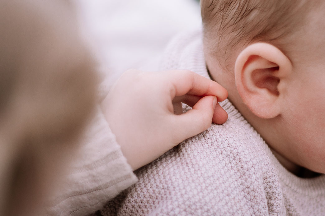 Eine Kinderhand die vorsichtig nach dem Ohr eines Babys greift. 