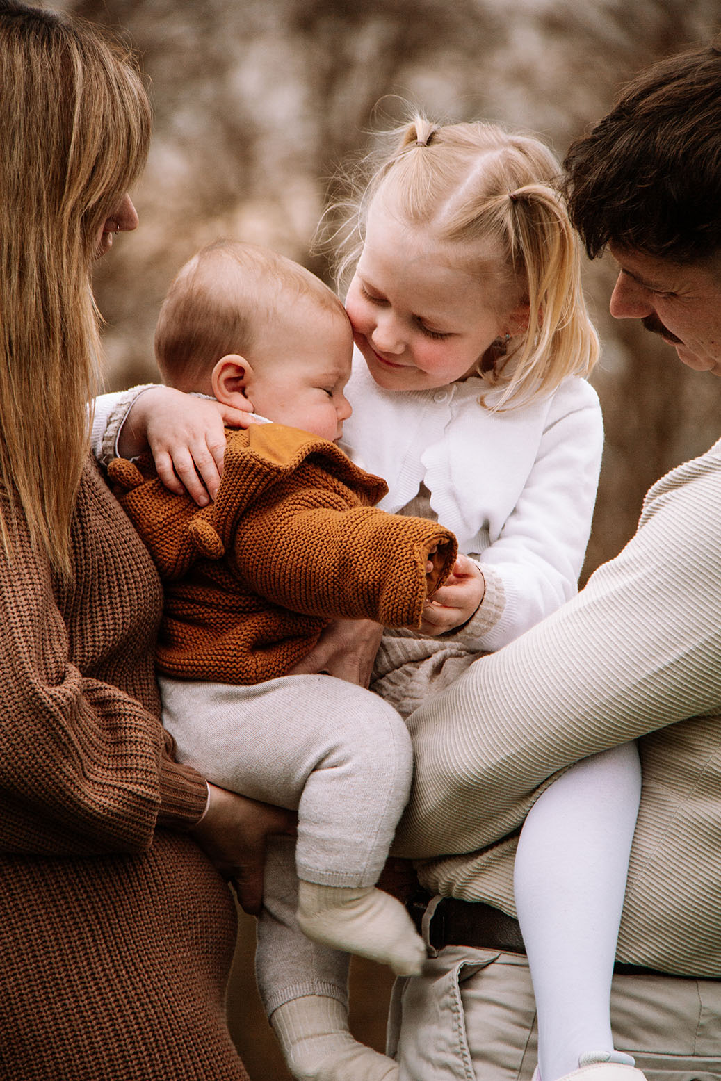 Eine Familie mit Mama, Papa; Babyjunge und einem Mädchen. Alle stehen nah beieinander. Die Kinder auf dem Arm der Eltern. Alle lächeln.