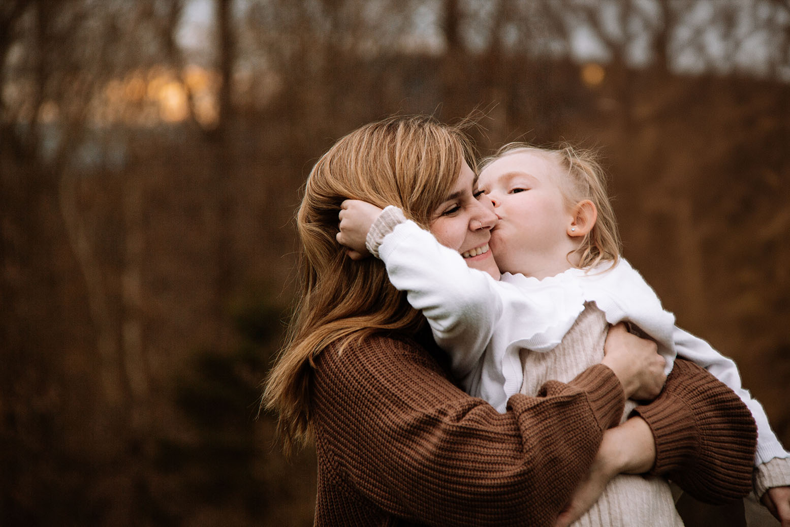 Eine Mutter, die ihr Mädchen in den Armen hält. Das Mädchen küsst die Backe der Mutter.