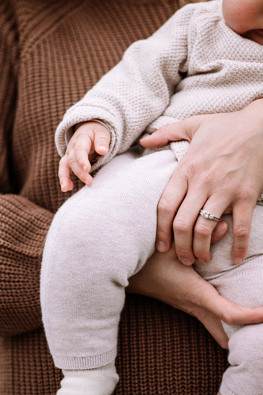 Ein Baby in den Armen der Mutter. Sie hält es fest. Man sieht die kleine Hand des Kindes.