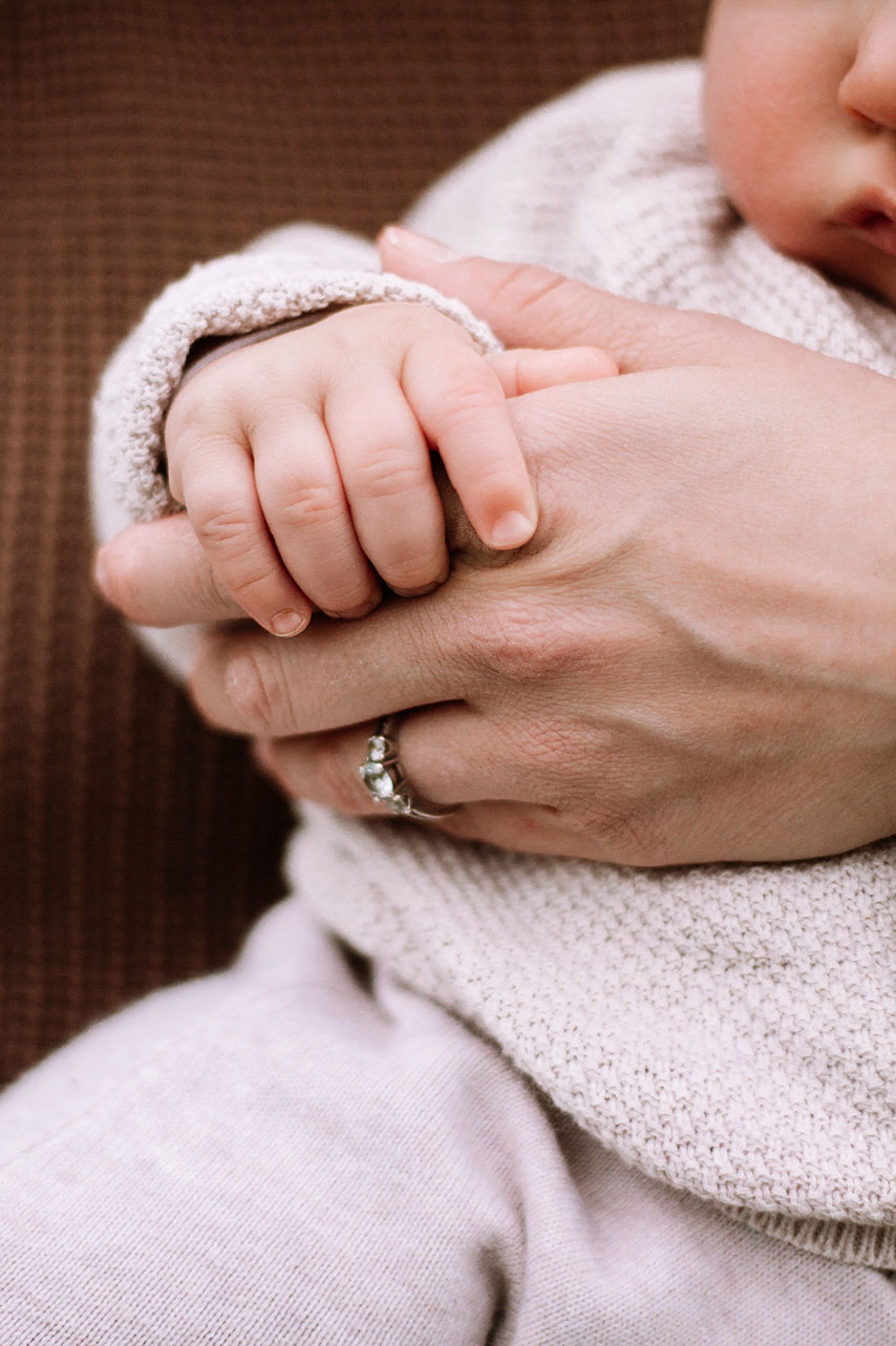 Ein Baby auf den Armen seiner Mutter. Man sieht eine Nahaufnahme der Hände. Das Baby greift nach den Fingern der Mutter.